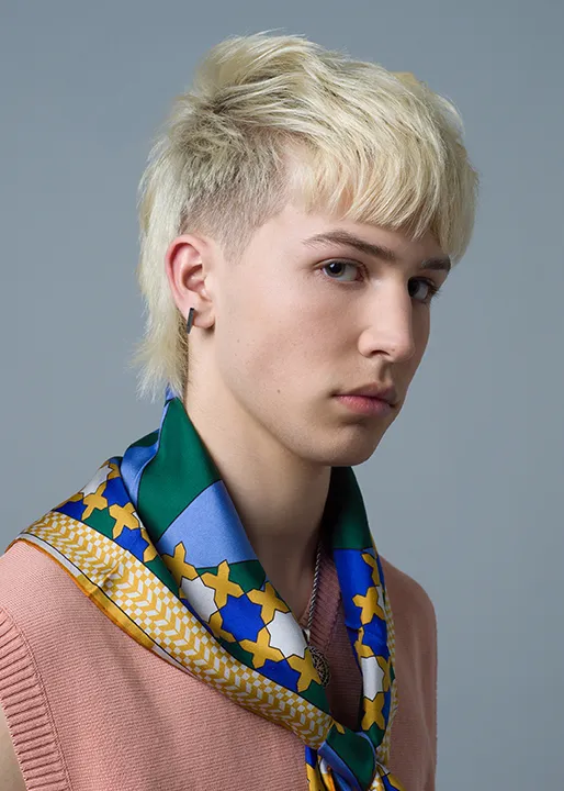 Blonde male model poses with fashionable Wave Fushion Mullet hairstyle.
