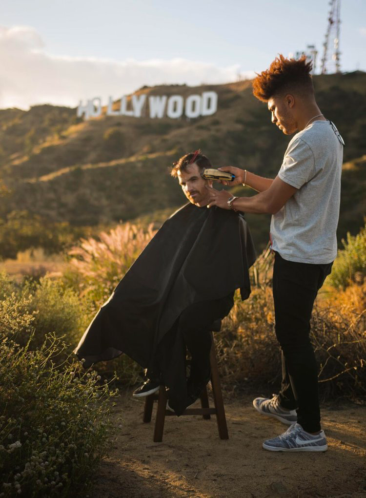 Julien Howard a.k.a. Velo Barber cutting a person's hair in the street